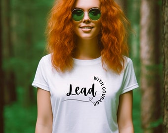 Peut inclure: T-shirt blanc avec l'inscription "Lead with Courage" en écriture noire. Le t-shirt présente un motif de cœur. La personne sur l'image porte des lunettes de soleil vertes et a les cheveux roux.