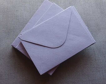 May include: A stack of three lavender envelopes with a textured surface.