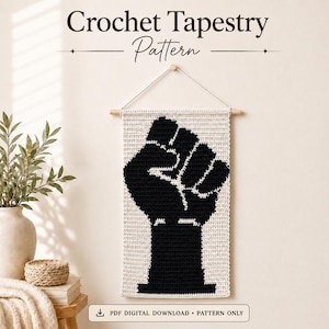 May include: A rectangular crochet tapestry featuring a black raised fist silhouette on a cream background. The piece hangs from a wooden dowel with a white cord. Text at the top reads Crochet Tapestry Pattern, and a bottom label reads PDF DIGITAL DOWNLOAD.