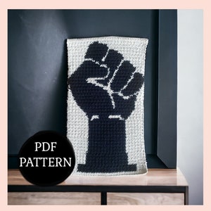 May include: A crochet pattern for a black fist raised in the air, with the words "PDF PATTERN" in a black circle below the image.