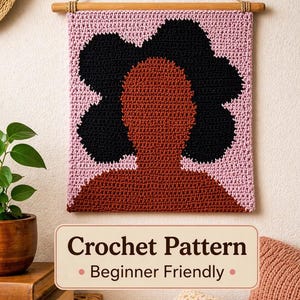 May include: A crochet wall hanging featuring a silhouette of a person with black hair and a brown face and neck, set against a pink background. The piece is suspended from a wooden rod with a rope. Text on the image reads "Crochet Pattern - Beginner Friendly."