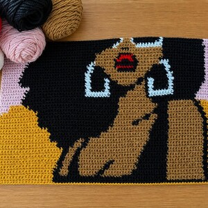 May include: A rectangular crochet tapestry featuring a graphic portrait of a person with dark skin, voluminous black hair, and large light blue hoop earrings. The figure has bright red lips and is set against a background of mustard yellow and light pink.