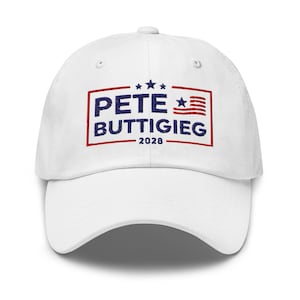 Könnte beinhalten: Eine weiße Baseballkappe mit gebogenem Schirm. Auf der Vorderseite steht der Name "PETE BUTTIGIEG" in Blau, mit einem rot-blauen Grafikdesign und dem Jahr "2028".