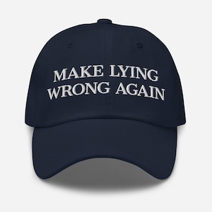 Może przedstawiać: Granatowa czapka bejsbolówka z białym haftem "MAKE LYING WRONG AGAIN". Czapka ma zakrzywiony daszek i guzik na górze.