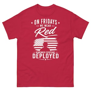 Puede incluir: Una camiseta roja con texto blanco y un gráfico de la bandera estadounidense. El texto dice: "ON FRIDAYS WE WEAR Red REMEMBER EVERYONE DEPLOYED."