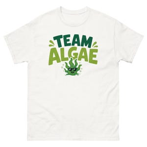 May include: A white short-sleeved t-shirt featuring a graphic print on the chest. The design includes the dark green text "TEAM" above the light green text "ALGAE" and a small green cartoon algae character wearing black sunglasses.