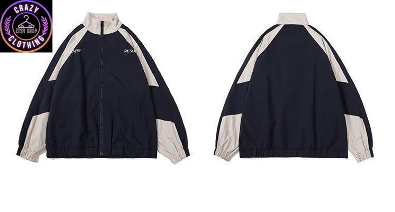 Op de afbeelding: Marineblauwe en beige trainingsjas met een volledige ritssluiting en een opstaande kraag. De jas heeft beige panelen op de schouders en mouwen, met de woorden "RESURE" en "RESURS" op de borst gedrukt. De jas heeft elastische manchetten en zoom.