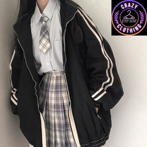 K&ouml;nnte beinhalten: Schwarze Jacke mit wei&szlig;en Streifen an &Auml;rmeln und Seiten, mit Rei&szlig;verschluss. Getragen &uuml;ber einem hellblauen Hemd, einer karierten Krawatte und einem karierten Faltenrock. Das Bild enth&auml;lt ein Logo mit der Aufschrift "Crazy Clothing Etsy Shop".