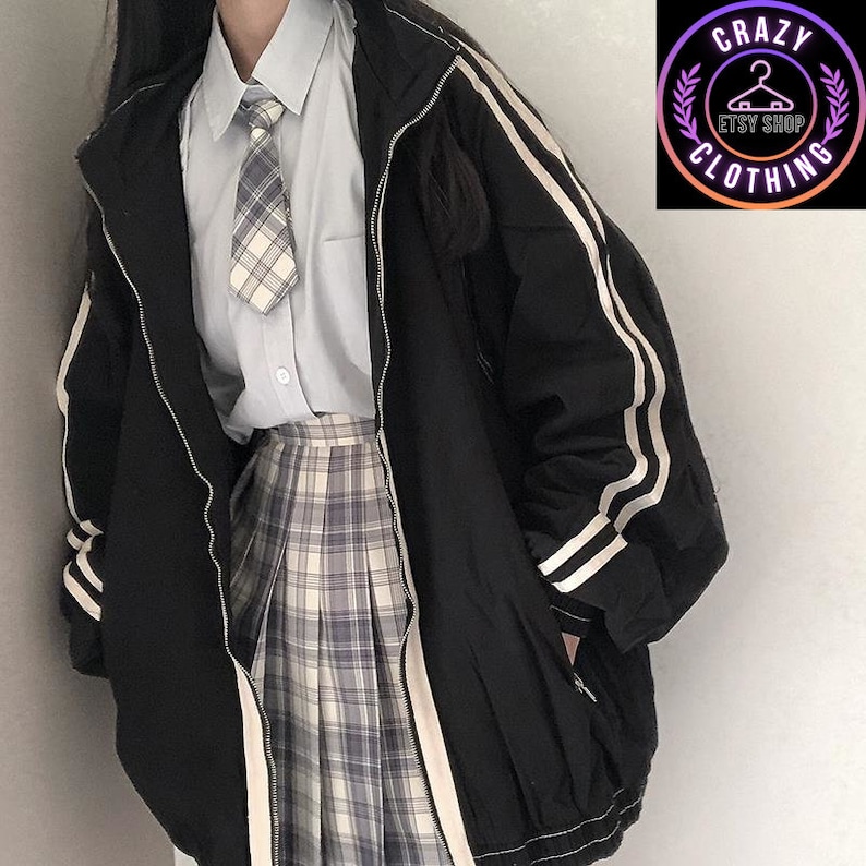 K&ouml;nnte beinhalten: Schwarze Jacke mit wei&szlig;en Streifen an &Auml;rmeln und Seiten, mit Rei&szlig;verschluss. Getragen &uuml;ber einem hellblauen Hemd, einer karierten Krawatte und einem karierten Faltenrock. Das Bild enth&auml;lt ein Logo mit der Aufschrift "Crazy Clothing Etsy Shop".