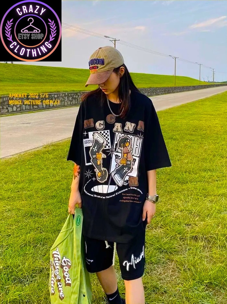 May include: Black t-shirt and shorts set with a graphic design featuring cartoon figures and the word "MCGANA". The outfit includes a brown and tan baseball cap. A green jacket with the text "Good Things are Gonna" is held in the hand.