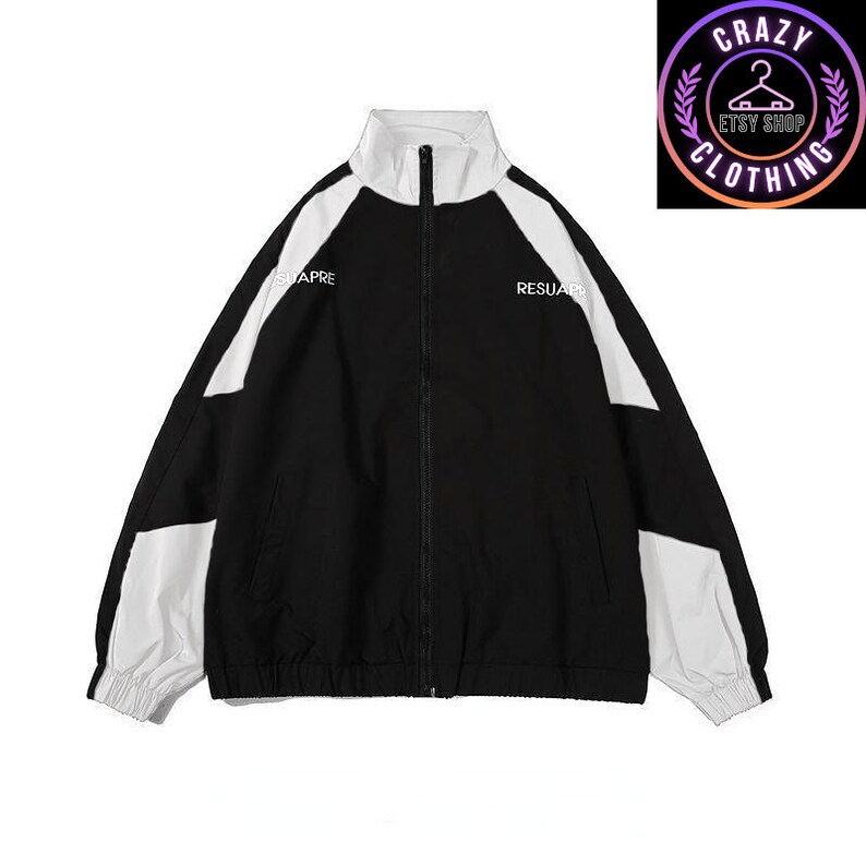 Op de afbeelding: Zwart-wit trainingsjack met een volledige ritssluiting en een hoge kraag. De jas heeft witte panelen op de schouders en mouwen, met de woorden "SUAPRE" en "RESUAR" op de voorkant. Het Etsy shop logo staat rechtsboven.