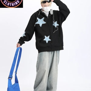 May include: Black zip-up hoodie with light blue star patches. The hoodie is paired with light wash denim jeans and a blue crossbody bag. The image includes the text "CRAZY CLOTHING ETSY SHOP" in a circular logo.