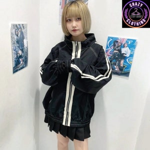 K&ouml;nnte beinhalten: Schwarze Jacke mit Rei&szlig;verschluss und wei&szlig;en Streifen an den &Auml;rmeln und vorne. Die Jacke hat einen hohen Kragen und elastische B&uuml;ndchen. Das Model tr&auml;gt einen schwarzen Faltenrock. Das Etsy-Shop-Logo "Crazy Clothing" befindet sich oben rechts.