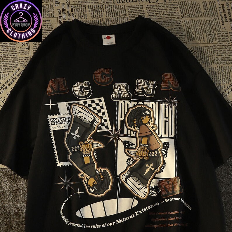 May include: Black t-shirt with a graphic design featuring two cartoon figures and the text "MCANN PRESERVED". The design includes stars, checkered patterns, and the phrase "The rules of our Natural Existence ~ Brother Mccann".