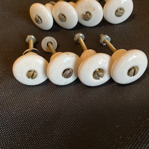 Peut inclure: Ensemble de boutons de meubles en céramique blanche avec des fixations métalliques. Les boutons sont ovales et ont une finition brillante. Les fixations métalliques comprennent des vis, des rondelles et des boulons.