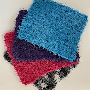 May include: Four different colored scrubby cloths stacked on top of each other. The top cloth is blue, the second is purple, the third is pink, and the bottom is black and white.