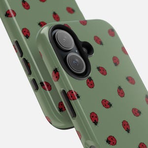 May include: Two green phone cases with a pattern of red ladybugs. The case on the right has a camera lens cutout.