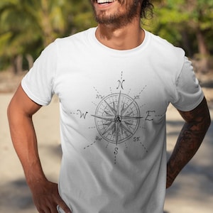 May include: A white t-shirt with a black and white compass design. The compass has the letters N, S, E, W, NE, NW, SE, and SW.