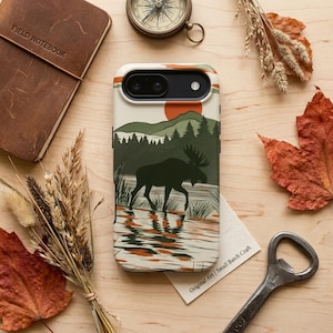 May include: A phone case with a nature scene featuring a moose in a lake, with a red sun and green trees. The case has a cream background with orange and green stripes. The text "Original Art | Small Batch Craft" is visible.