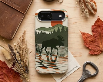 Puede incluir: Funda de teléfono con una escena de la naturaleza que presenta un alce en un lago, con un sol rojo y árboles verdes. La funda tiene un fondo crema con rayas naranjas y verdes. El texto "Original Art | Small Batch Craft" es visible.