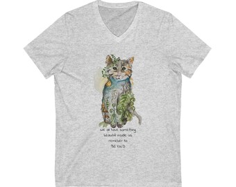Puede incluir: Una camiseta gris claro con cuello en V con una ilustración de acuarela de un gato adornado con plantas. La ilustración del gato tiene una combinación de colores azul claro y verde. El texto "We all have something beautiful inside us, remember to BE KIND" está debajo.