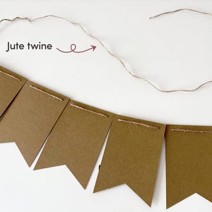 Op de afbeelding: Een banner bestaande uit zes bruine rechthoekige kartonnen vlaggetjes met zwaluwstaartvormige onderkanten, geregen aan een stuk jute touw. De tekst Jute twine staat boven het touw met een pijl die naar het koord wijst.