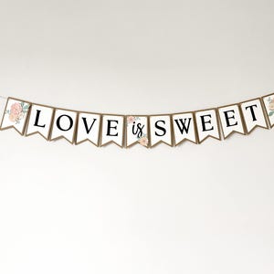Op de afbeelding: Een decoratieve slinger bestaande uit individuele witte vlaggetjes met bruine randen, die de tekst LOVE IS SWEET vormen in zwarte hoofdletters. De twee buitenste vlaggetjes en het middelste vlaggetje zijn versierd met illustraties van roze bloemen.
