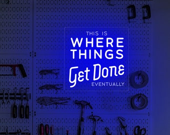 Puede incluir: Un letrero de neón azul con texto blanco que dice "This is where things get done eventually". El letrero está montado en una pared de tablero de clavijas blanco con varias herramientas colgadas.