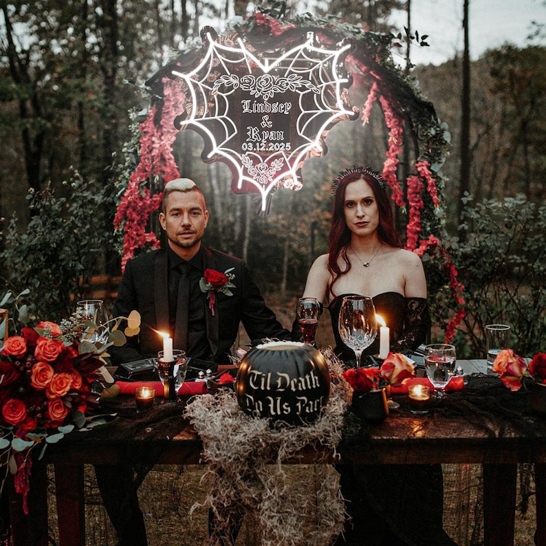 Peut inclure: Une table de r&eacute;ception de mariage avec une citrouille noire sur laquelle est inscrit "Til Death Do Us Part" et une enseigne au n&eacute;on en forme de c&oelig;ur avec une toile d'araign&eacute;e qui dit "Lindsey & Ryan 03.12.2025".