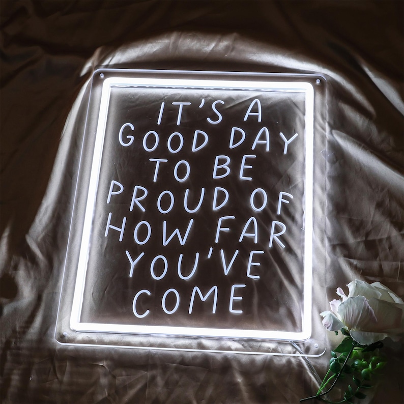 May include: White neon sign with the text "It's a good day to be proud of how far you've come".