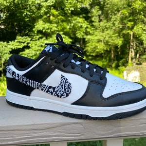 May include: Black and white Nike low-top sneakers with a paisley pattern on the swoosh and side panel. The shoes have black laces and a white midsole.