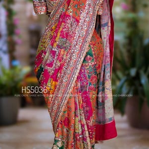 May include: A multi-colored crepe saree featuring intricate embroidery, mirror work, and a patchwork-style floral pattern in shades of pink, orange, and green. The garment includes a matching blouse and is labeled with the text HS5036.
