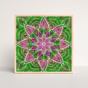 Könnte beinhalten: Ein quadratisches Wandbild mit einem leuchtenden Mandala-Design in Magenta, leuchtendem Grün und Weiß. Das komplexe Muster besteht aus geschichteten Blütenblättern und geschwungenen Linien, eingefasst in einen hellen Holzrahmen.