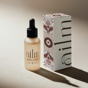 May include: A glass bottle with a dropper filled with a clear liquid. The bottle is labelled "ailm" and "Health & Beauty". The bottle is sitting on a white surface next to a white box with a floral design and the word "ailm" printed on it.