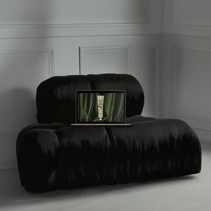 Op de afbeelding: Een zwarte, gestoffeerde bank met een laptop erop. Het laptopscherm toont een groene achtergrond met een tube crème erop. De tekst op de crèmetube luidt "LOVE".