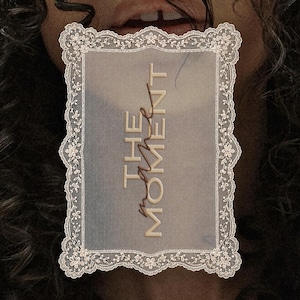 May include: A rectangular, semi-transparent card featuring an intricate, cream-coloured lace border with floral patterns. The text THE MOMENT is printed in a bold, sans-serif font, with the word MAKE written in a cursive script over it.