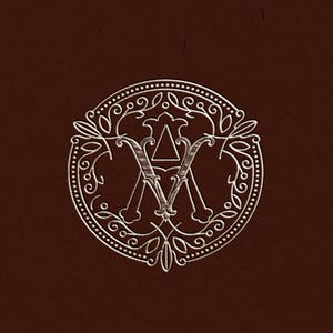 May include: A detailed, circular emblem with the intertwined letters "A" and "V" in a decorative, vintage style. The design is white on a dark brown background, featuring ornate floral and dotted border elements.