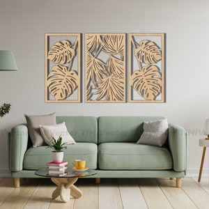 May include: Three wooden wall panels with a cutout design of tropical leaves. The panels are arranged horizontally and are mounted on a white wall. A green sofa with pillows is in the foreground.