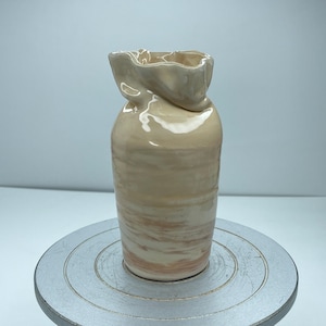 May include: A ceramic vase with a light brown glaze and a ruffled top. The vase has a marbled effect with streaks of pink and white.