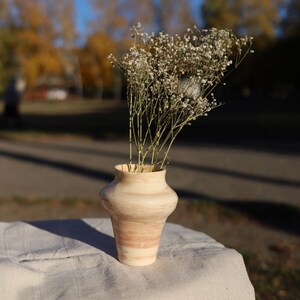 May include: A white ceramic vase with brown stripes, filled with white baby's breath flowers, sits on a white linen tablecloth.