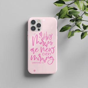 Puede incluir: Funda de teléfono rosa claro con la frase "His mercies are new every morning" en rosa brillante. El texto es de Lamentaciones 3:23. La funda tiene un recorte para la cámara y un pequeño punto en la parte inferior.