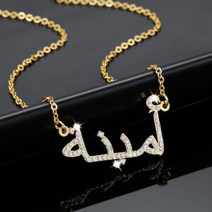 May include: Gold chain necklace with a pendant featuring the Arabic word "Habibi" in sparkling rhinestones.