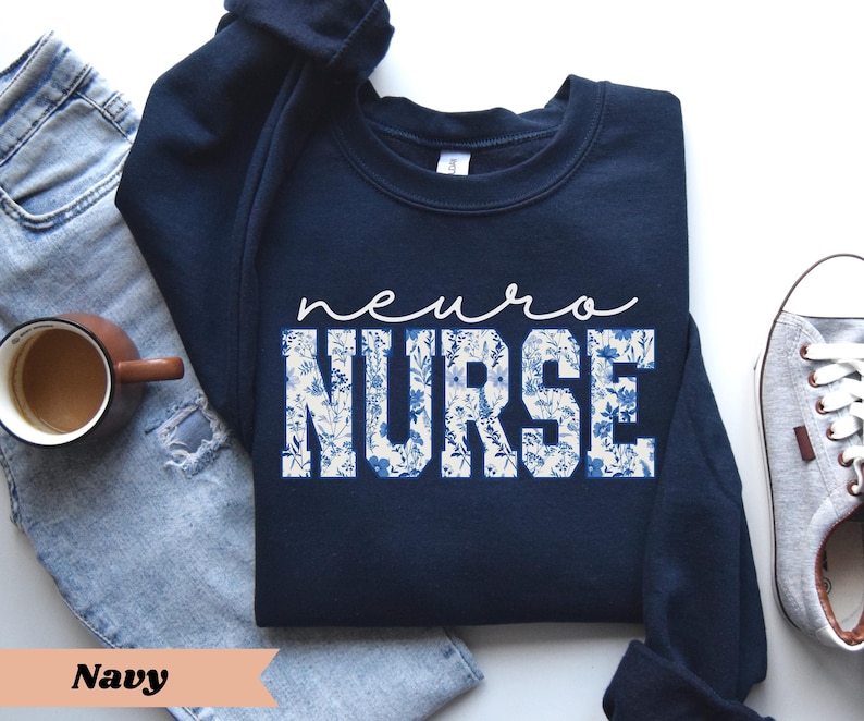 Puede incluir: Sudadera azul marino con un dise&ntilde;o floral blanco y el texto "neuro nurse".