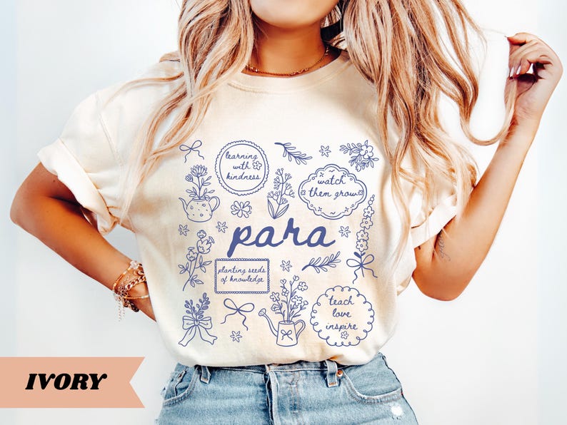 May include: An ivory t-shirt featuring a blue graphic print with the word "para" in the center, surrounded by illustrations of flowers, a watering can, a teapot, and text bubbles reading "learning with kindness," "watch them grow," and "teach love inspire."