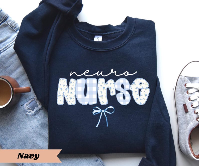 May include: Navy blue sweatshirt with the words "neuro nurse" in white script and block letters. The word "nurse" has a blue gingham pattern with small floral accents. A light blue bow is below the word "nurse".