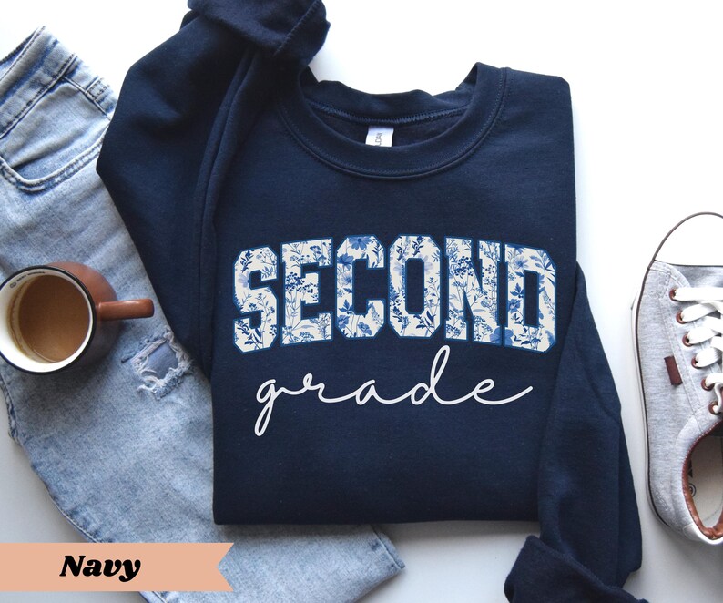 May include: Navy blue sweatshirt with a white floral design that says "Second Grade".