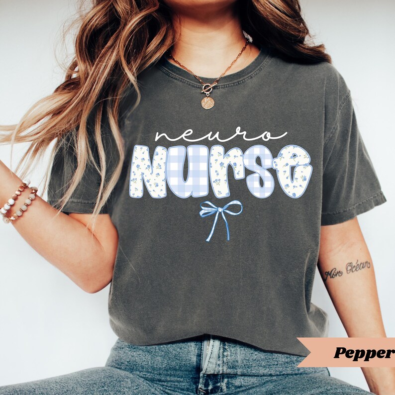 May include: A dark gray t-shirt with the words "neuro nurse" in white script. The word "nurse" is in a blue gingham pattern with small floral accents. A blue bow is below the word "nurse".