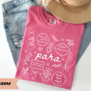 May include: A pink t-shirt featuring white line art illustrations of flowers, watering cans, and bows. The text reads: learning with kindness, watch them grow, para, planting seeds of knowledge, and teach love inspire in various frames.