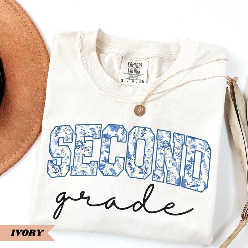 May include: Ivory t-shirt with a blue floral print that says "Second Grade" in a vintage style font.