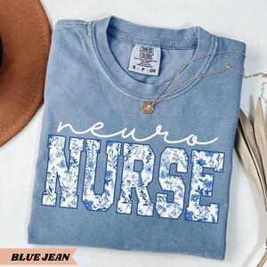 Puede incluir: Una camiseta azul vaquero con un dise&ntilde;o floral blanco que dice "neuro nurse".